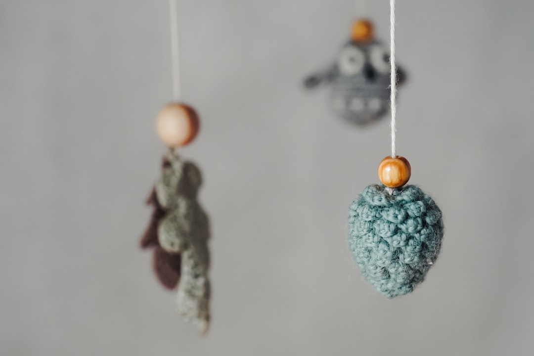 Crocheted ornaments with wooden beads hanging on strings against a plain, light background.