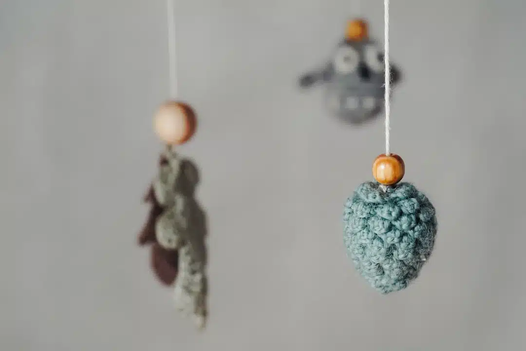 Crocheted ornaments with wooden beads hanging on strings against a plain, light background.