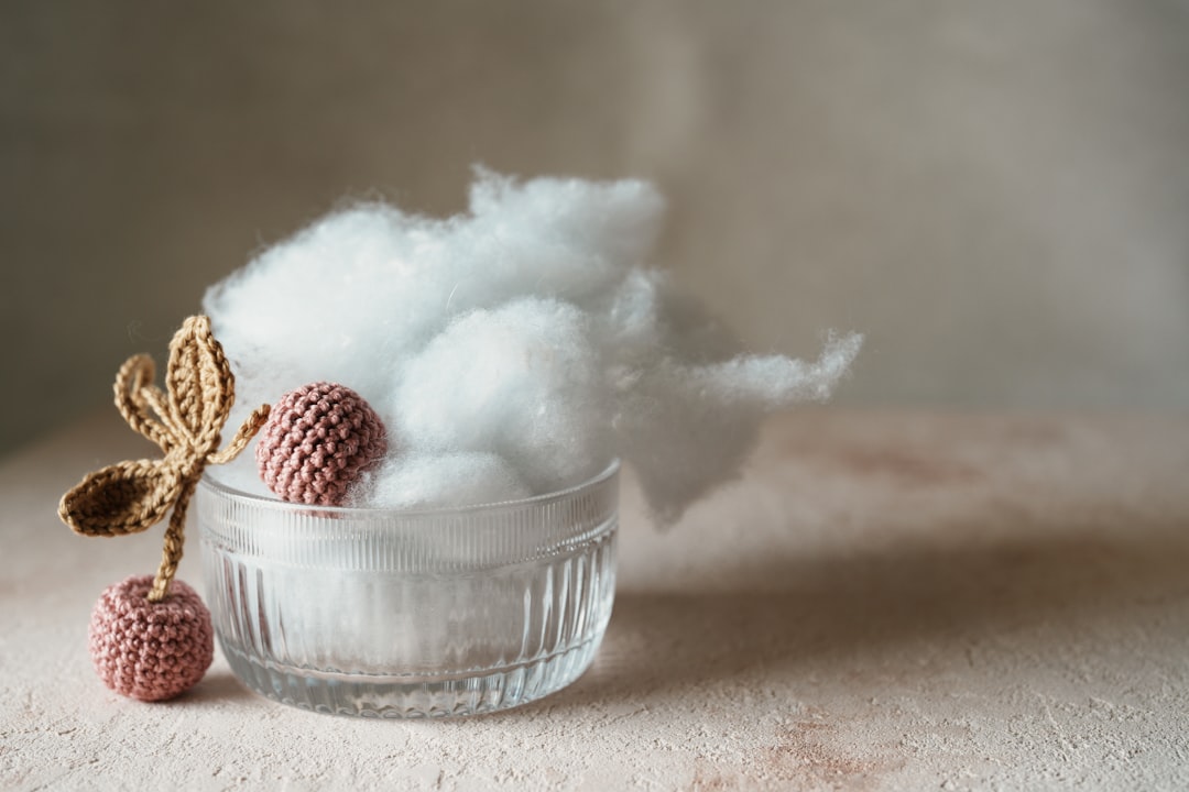 Glass bowl with white cotton-like stuffing, crocheted pink cherries, and a crocheted brown leaf on a beige surface.