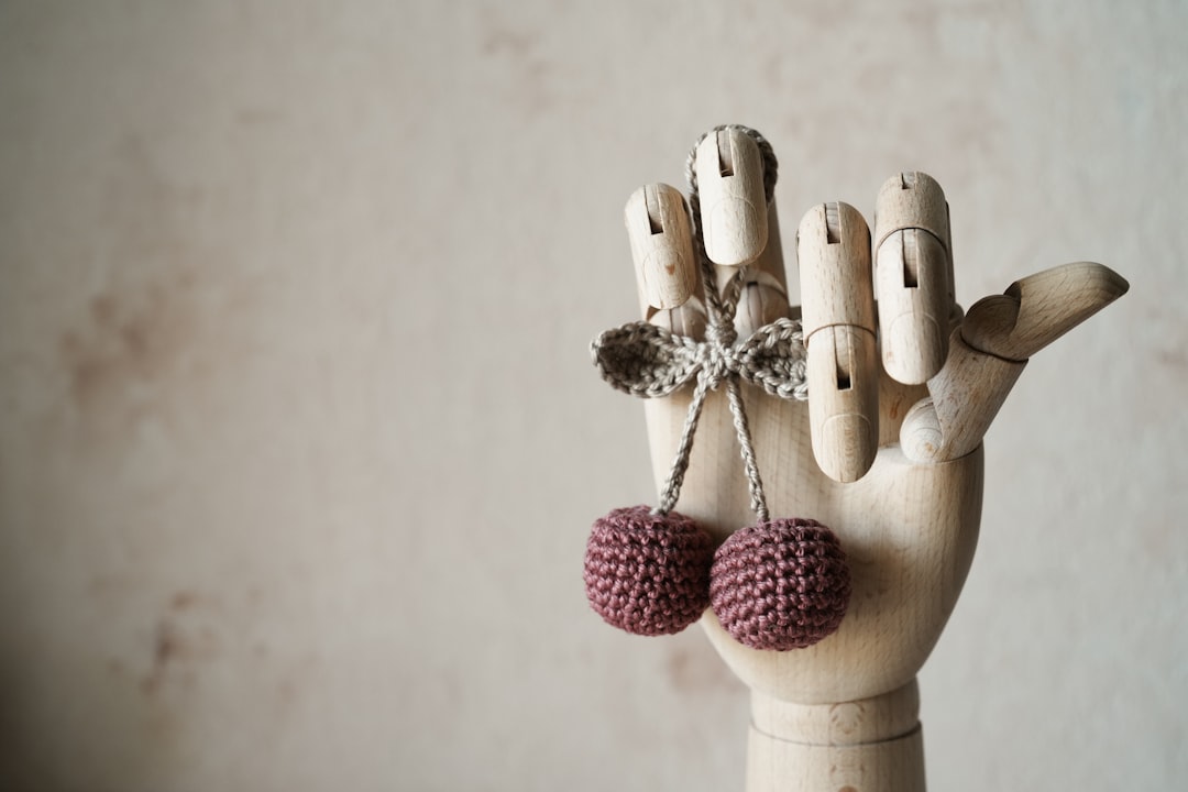 A wooden mannequin hand displays two crocheted cherries tied with a string against a neutral background.