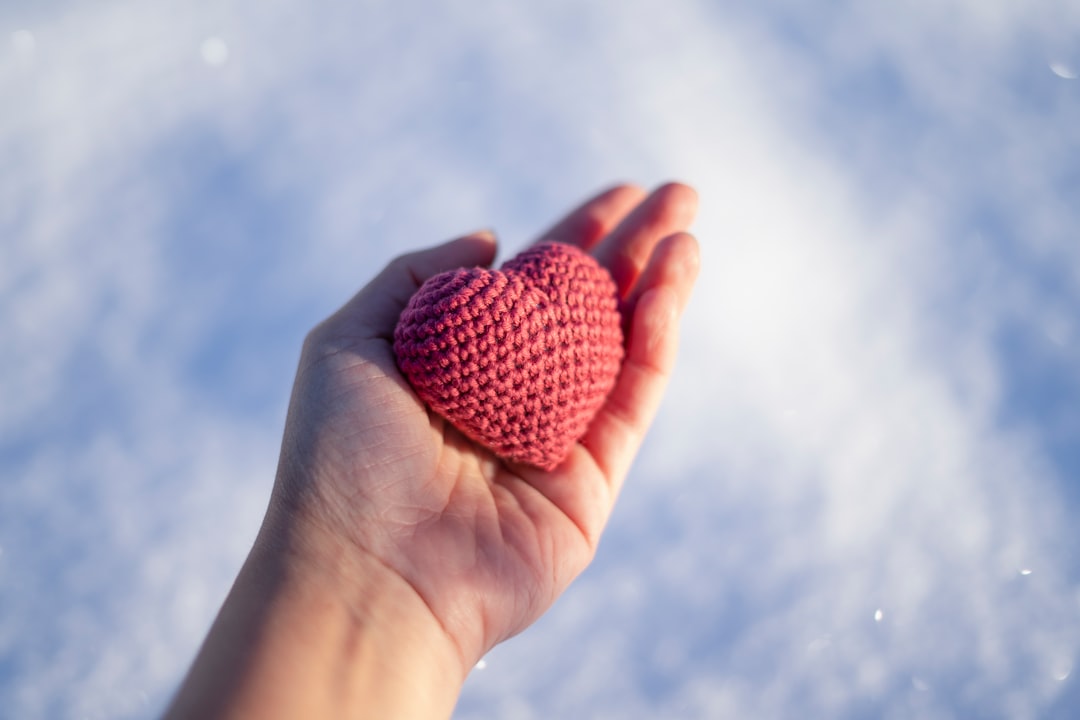 A hand holding a knitted red heart against a snowy, blurred background.