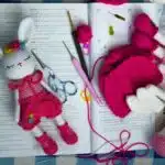 Crocheted bunny doll and parts, crochet hooks, yarn, and an open instruction book on a table.