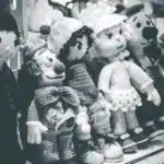 Black and white photo of various hand-knitted dolls arranged in a row on a shelf.