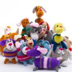 A group of colorful crocheted animal toys, including dogs and cats, arranged together on a white background.