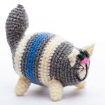 A knitted, striped cat figurine with blue, gray, and cream colors on a white background.
