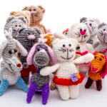 Group of colorful crocheted animal dolls, including cats, a dog, and a rabbit, on a white background.