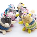 Six colorful crocheted cat dolls arranged in a circle on a white background.