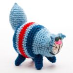 A crocheted blue cat plush toy with red and white stripes and a large tail, standing on four legs.