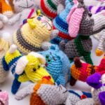 Colorful crocheted animal toys are scattered closely together on a white surface.