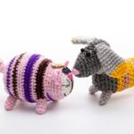 Crocheted pink cat and gray dog facing each other on a white background.